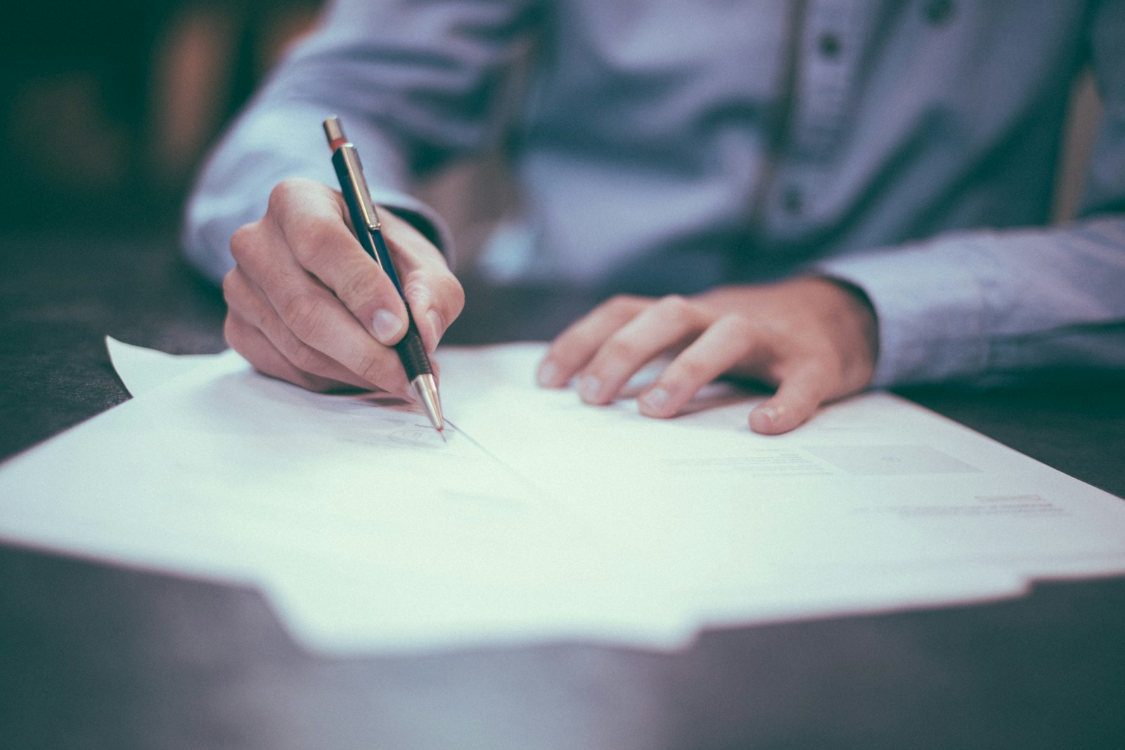 A signatory's hand with pen over a contract
